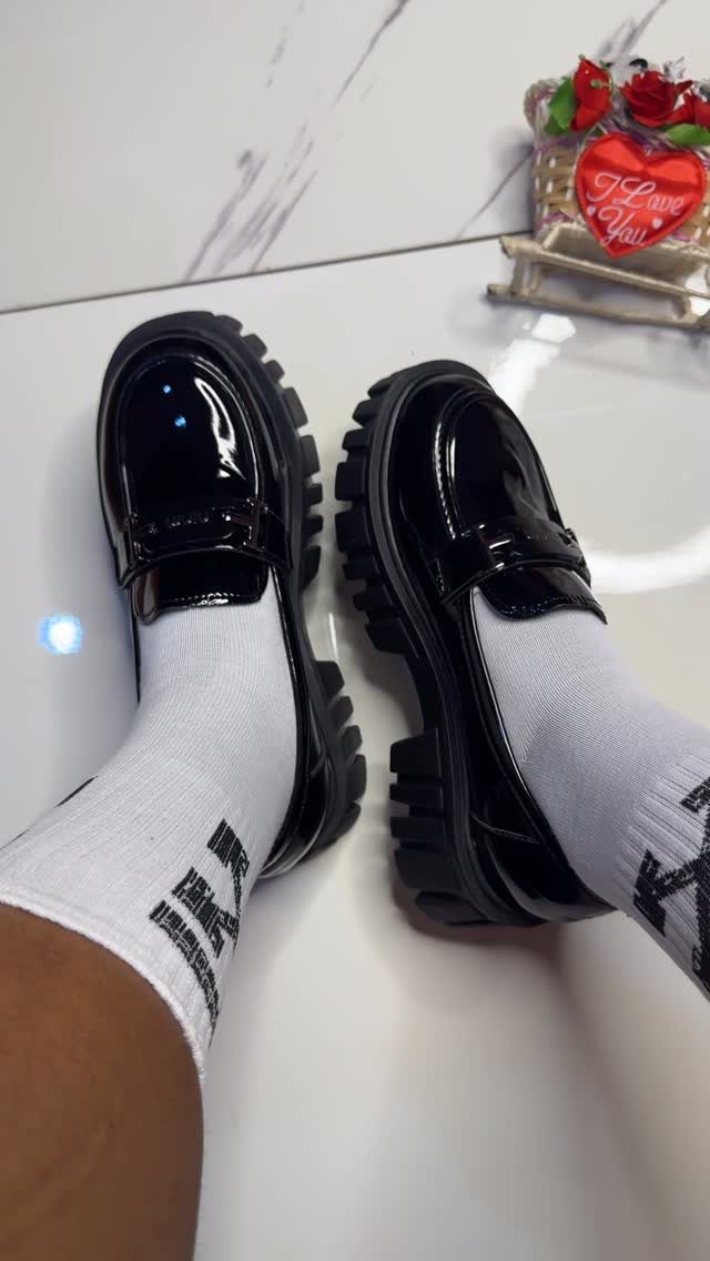 Black patent leather chunky platform loafers worn with white crew socks on a marble floor.