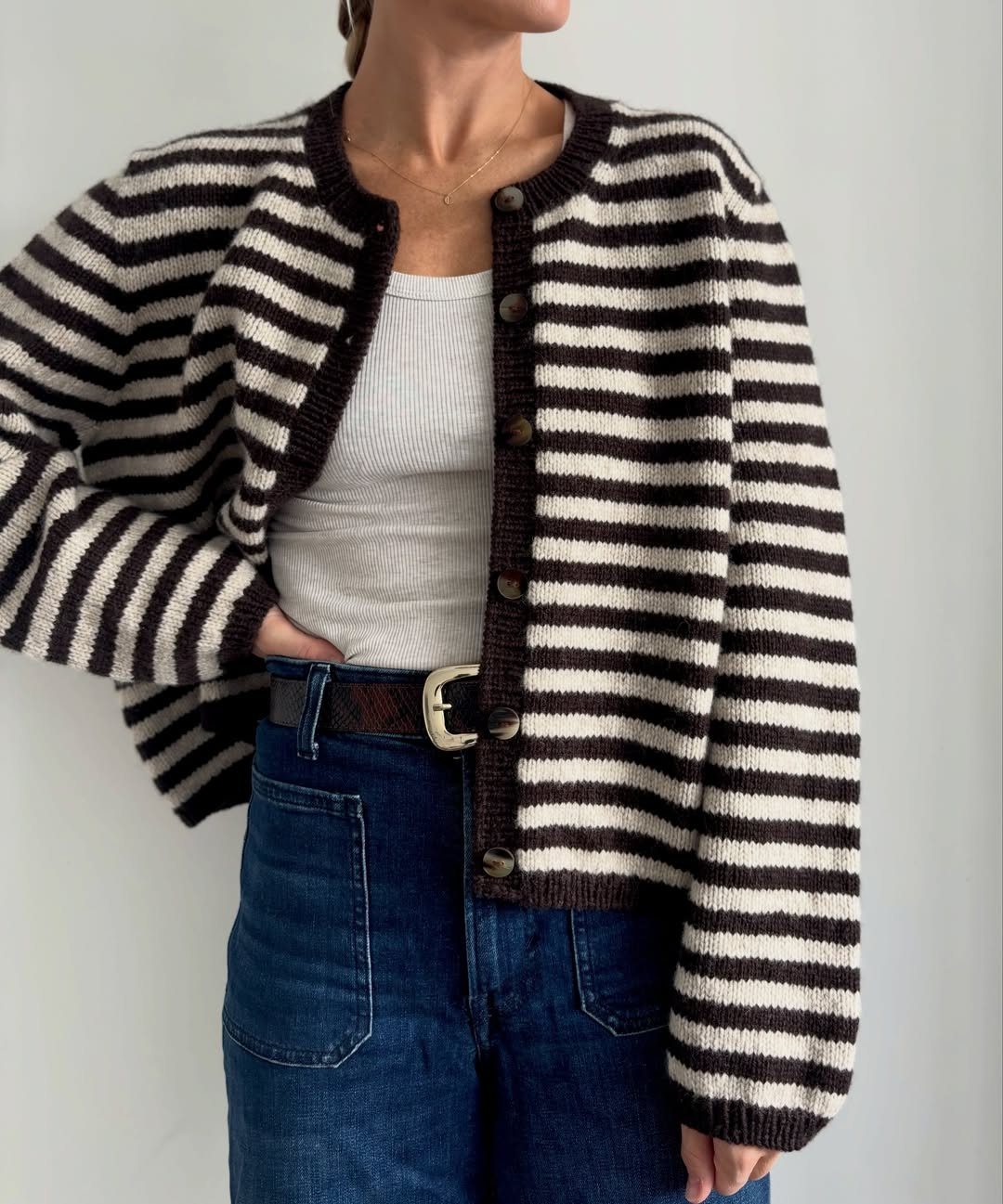 A person wearing a brown and white striped cardigan over a white tank top and blue jeans.