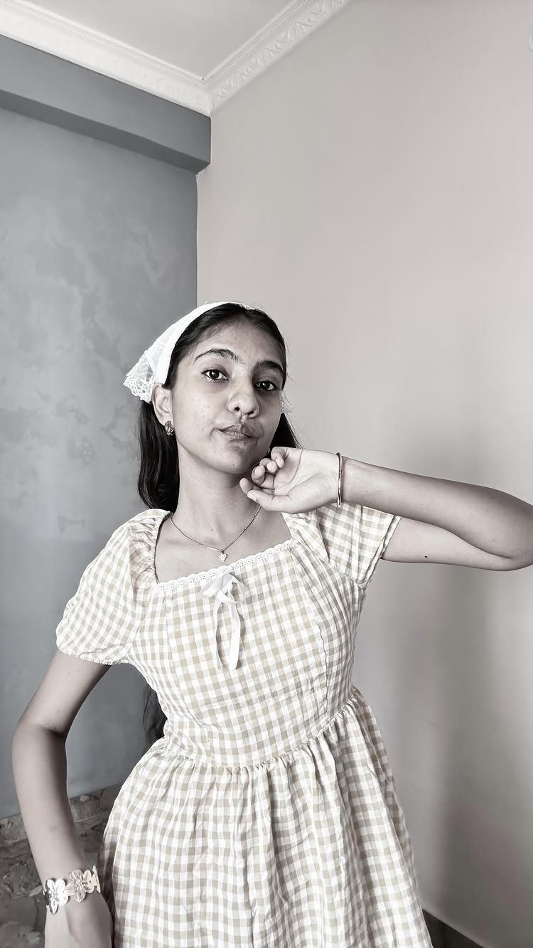 A young woman posing in a gingham patterned dress with a white headband.