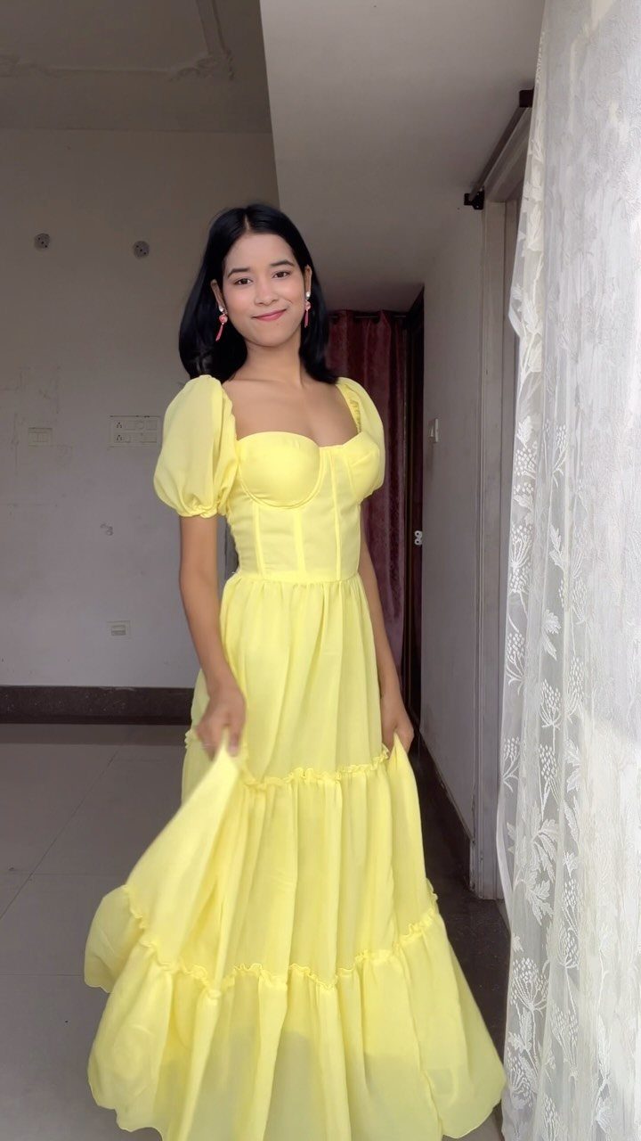 A young woman posing in a long, bright yellow puff-sleeve dress indoors.