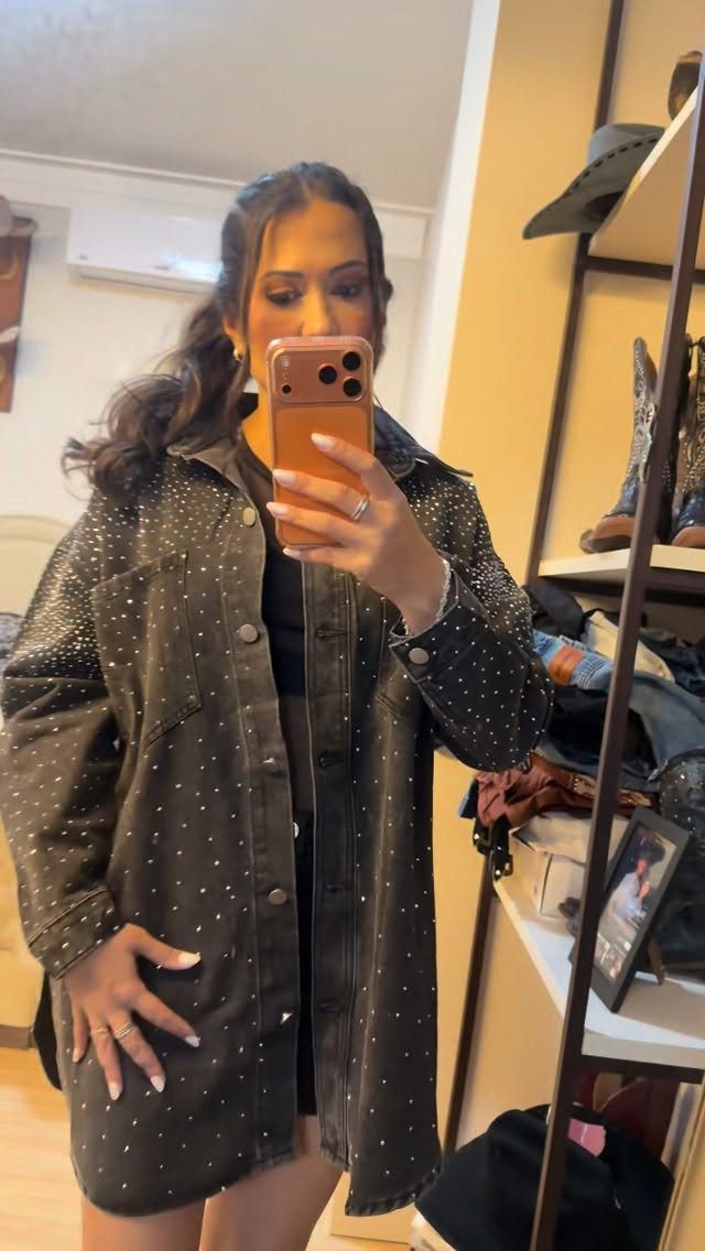 Woman in a black rhinestone-embellished denim jacket taking a mirror selfie.