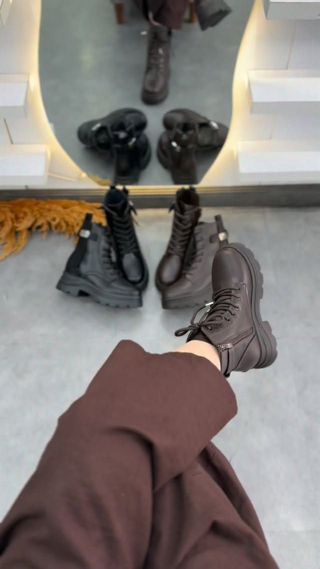 Several pairs of chunky black and brown ankle boots arranged on a light grey floor.