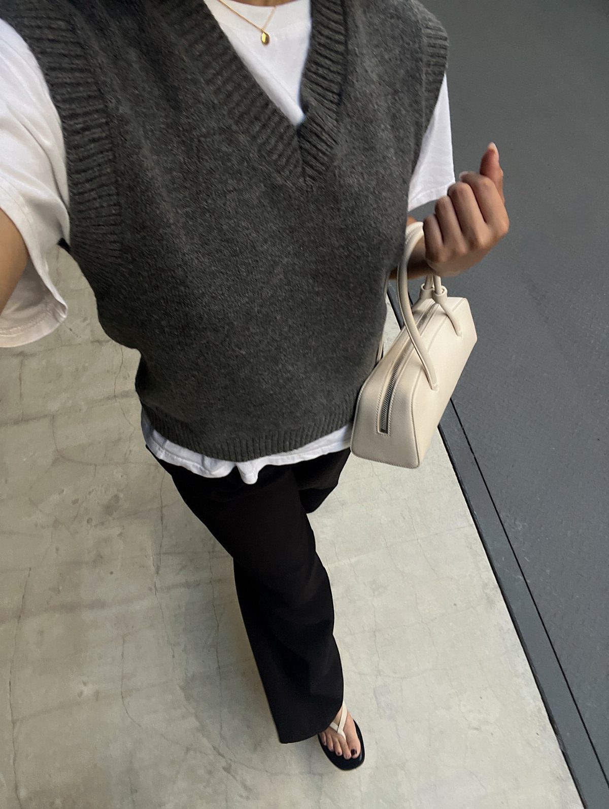 A person wearing a grey knit vest over a white shirt and black pants.