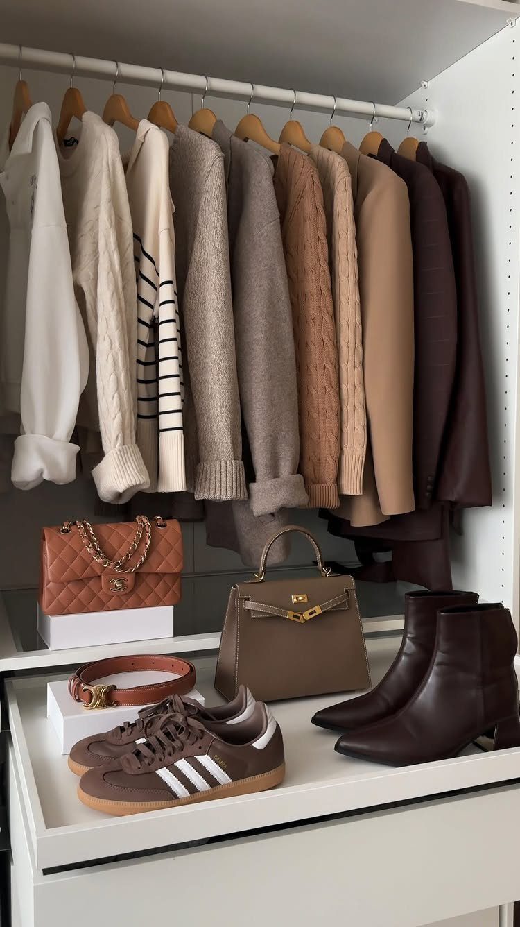 Neutral toned sweaters, shirts, and accessories arranged neatly on a white closet shelf and hanging rod.