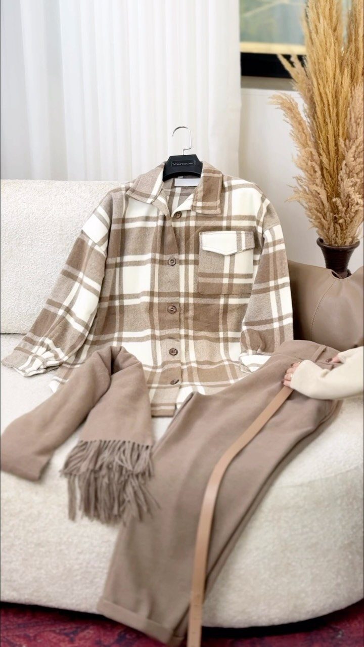 A beige and white plaid shacket hanging on a sofa with matching tan accessories.