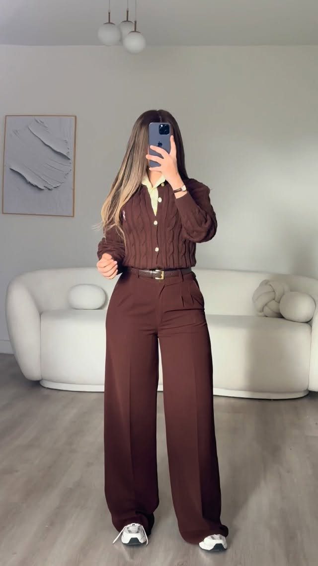 A person wearing brown wide-leg trousers, a matching cardigan, and white sneakers in a bright room.