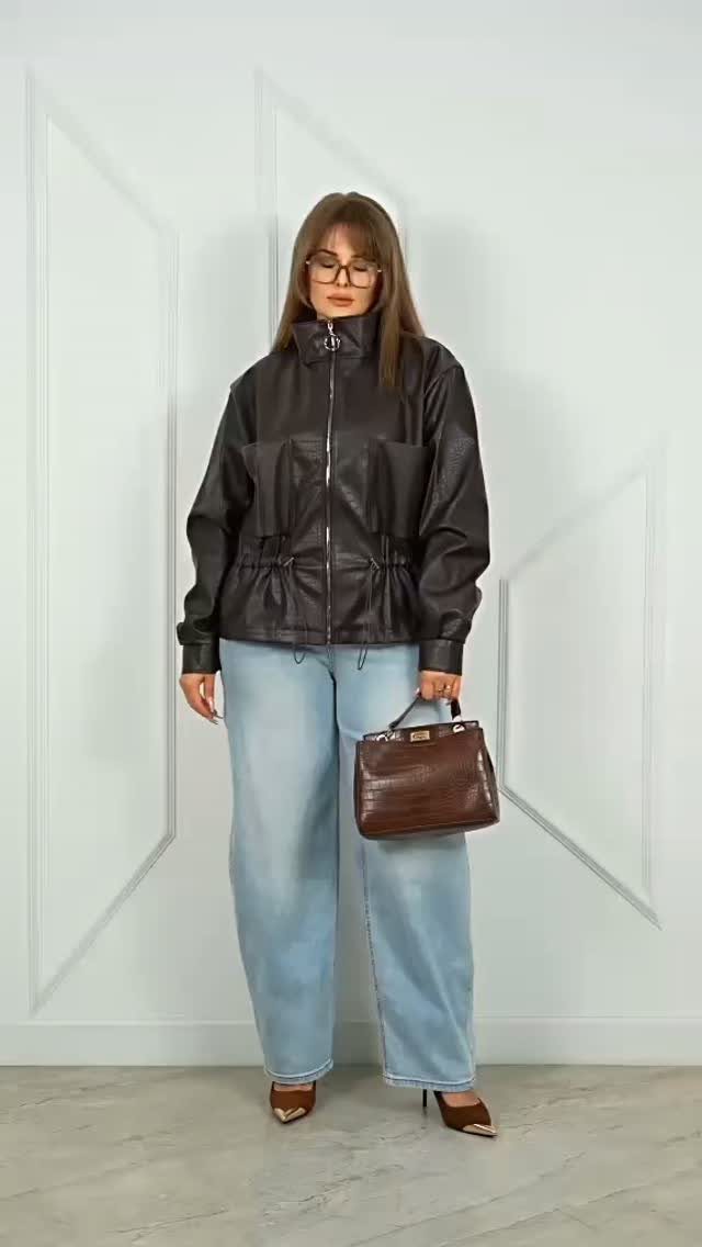 A woman wearing a dark leather jacket and wide-leg jeans holding a brown handbag.
