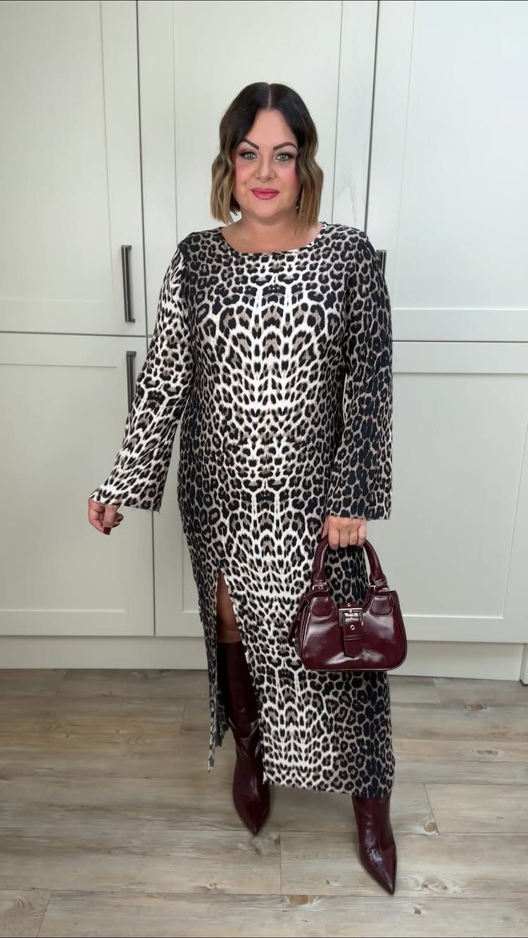 A woman in a leopard print maxi dress and burgundy boots posing in a kitchen.