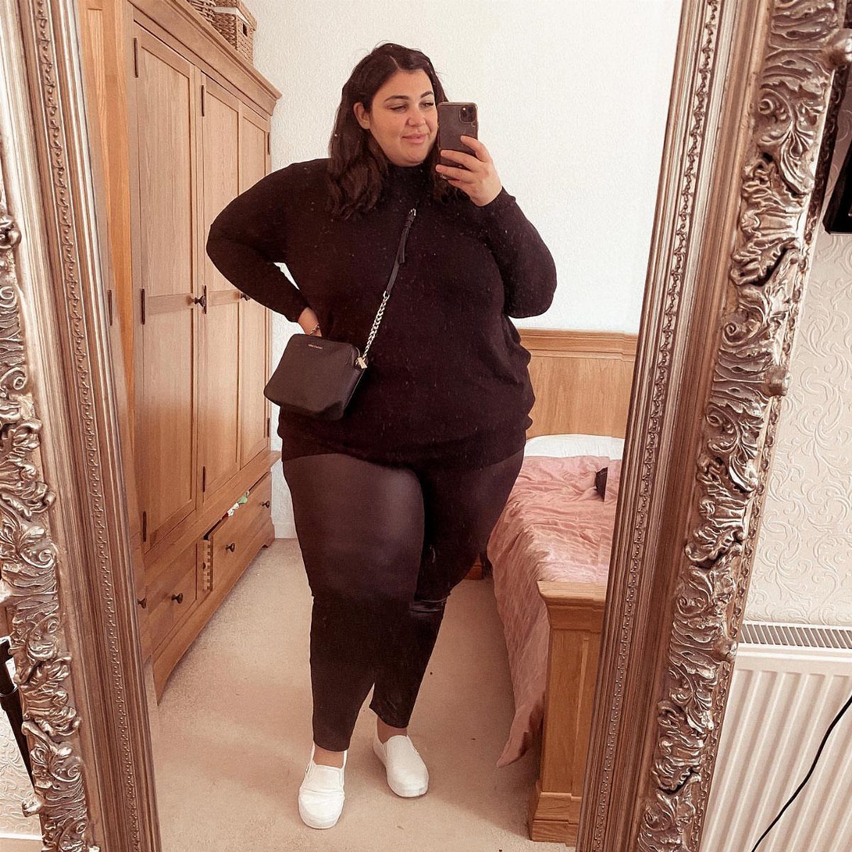 Woman in a black tunic sweater and dark leggings posing for a mirror selfie.