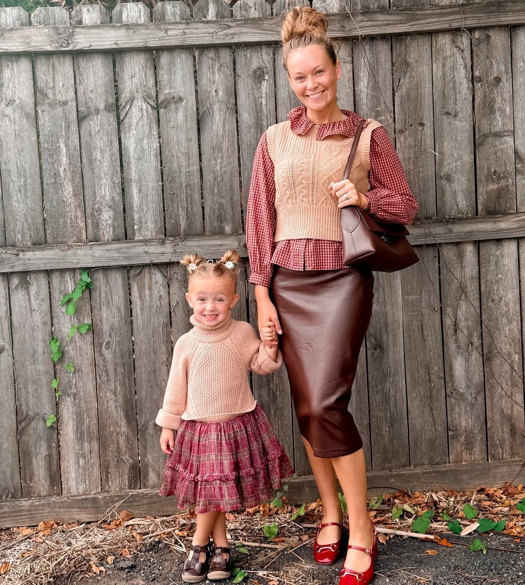 A woman and a young girl posing together in front of a weathered wooden fence.