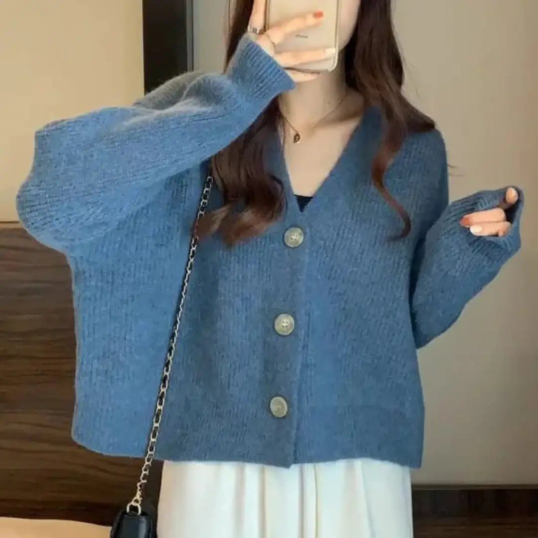 A person wearing a blue knit v-neck cardigan and white top taking a mirror selfie.