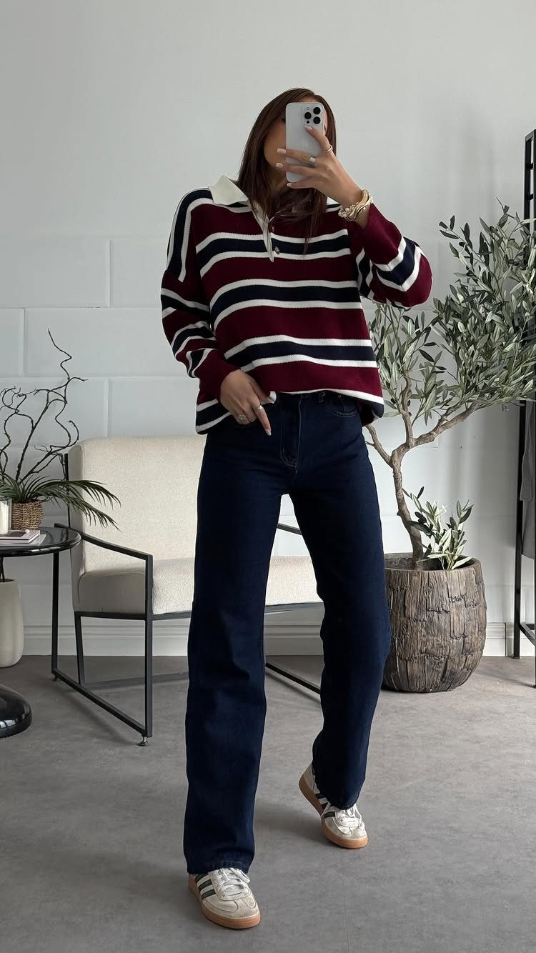 A person wearing a striped sweater and dark wash jeans posing for a mirror selfie.