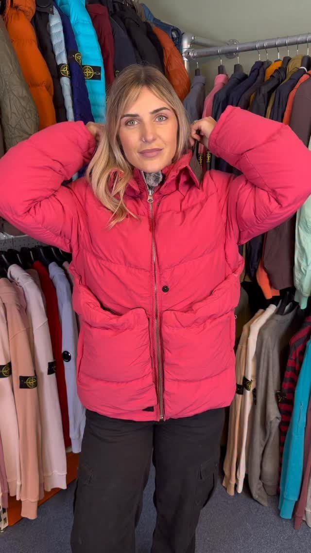 A woman posing in a bright pink puffer jacket in front of a clothing rack.