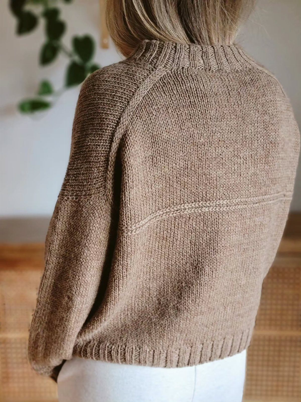 A person wearing a textured brown knitted sweater with a ribbed collar and hem.