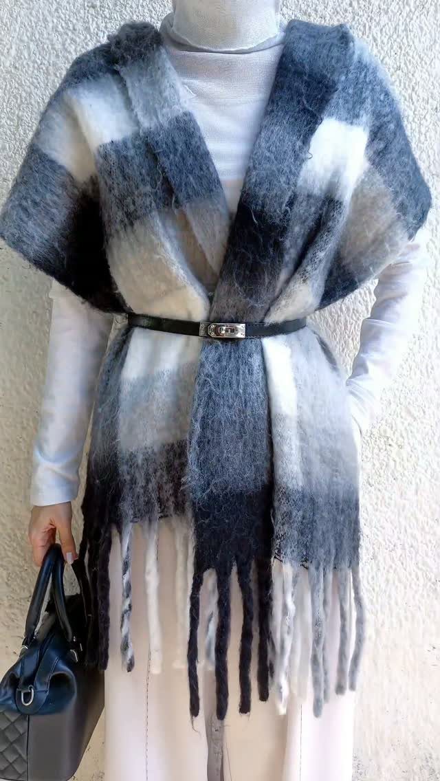 A person wearing a large grey and white checkered wool wrap belted at the waist.