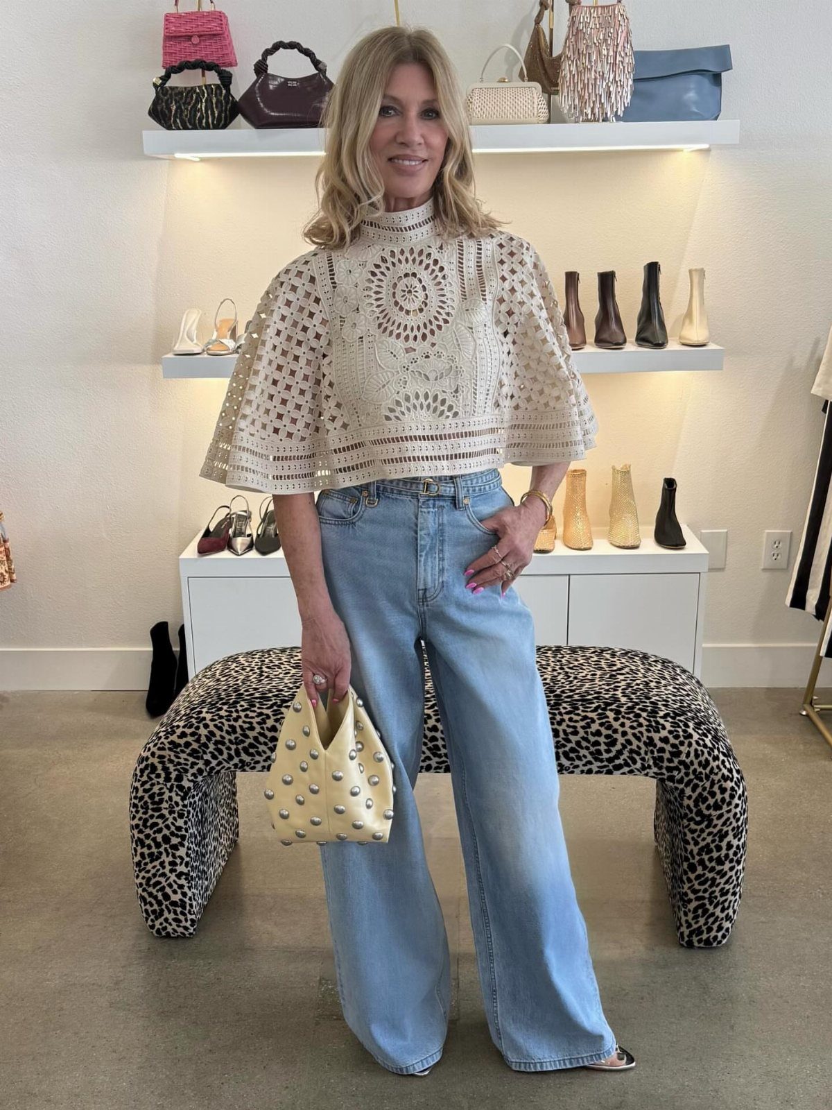 Woman wearing light blue baggy jeans and a cream crochet lace capelet top standing in a boutique.