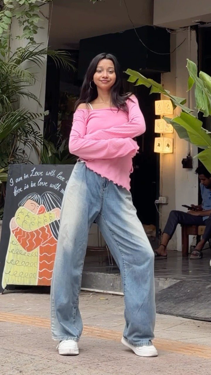A woman posing in light blue baggy jeans and a pink long-sleeved top outdoors.