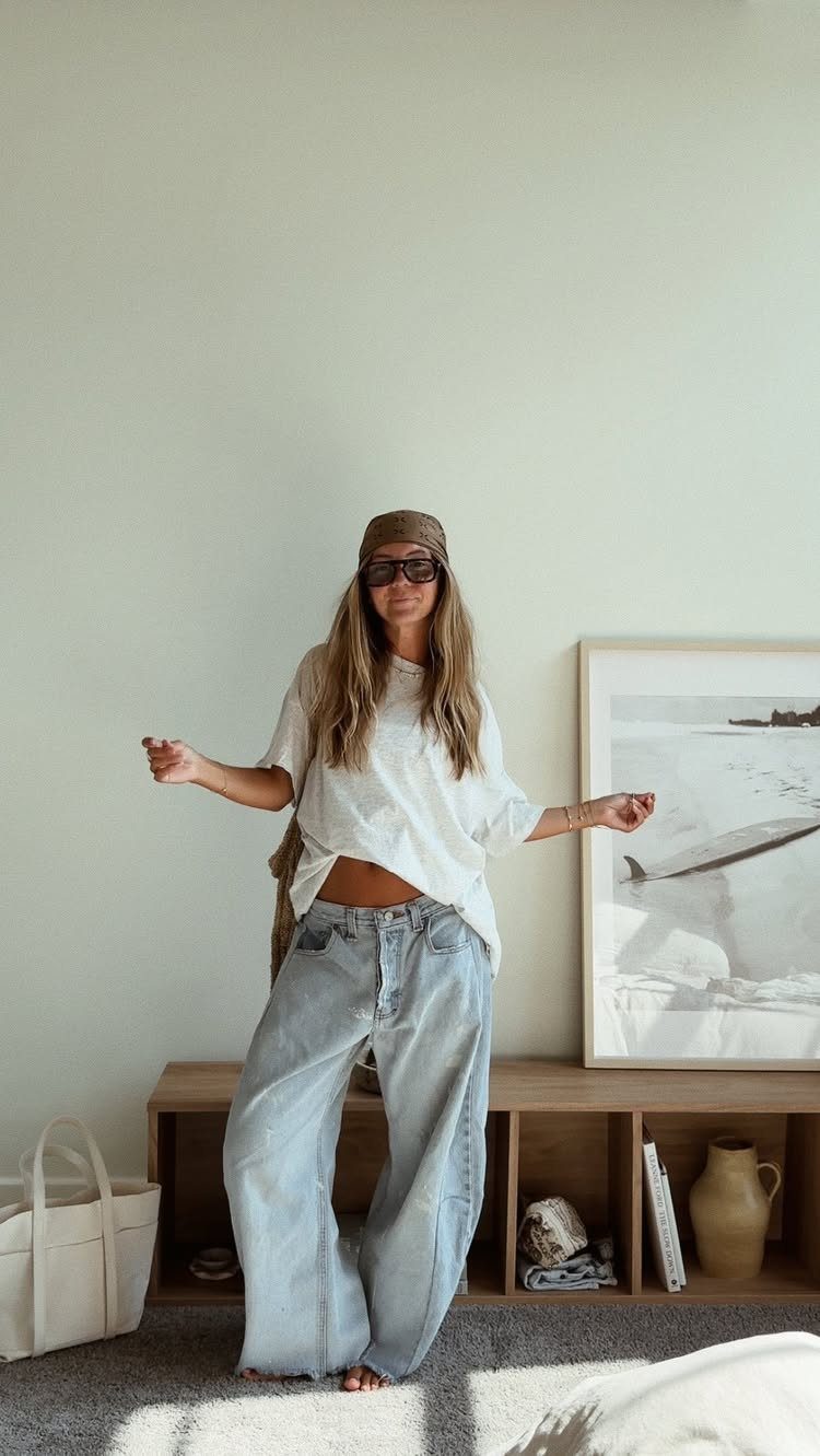 Woman wearing light blue baggy jeans and a white oversized t-shirt with a brown headscarf.