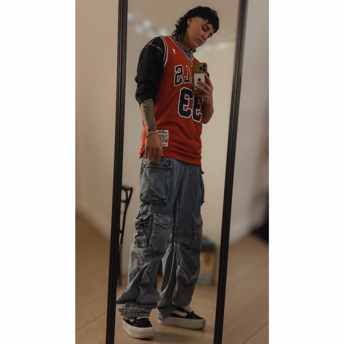 Person in an orange sports jersey and baggy denim cargo jeans taking a mirror selfie.