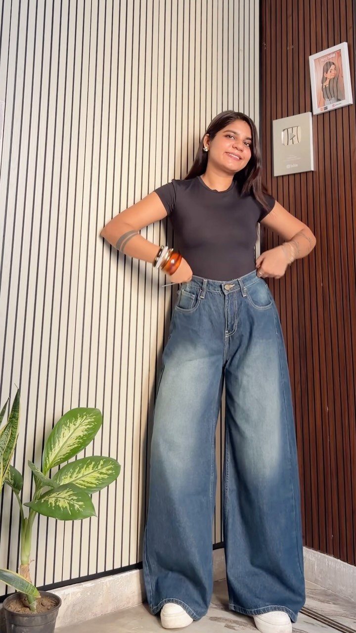 A woman wearing dark grey fitted top and extremely wide-leg blue denim jeans.