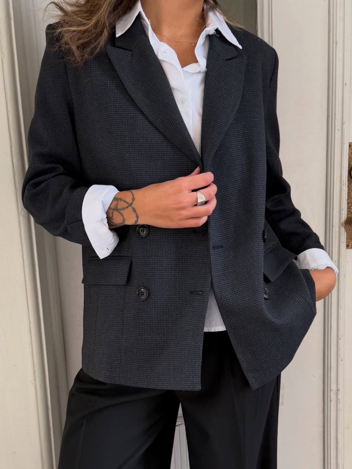 A person wearing a black textured blazer over a white collared shirt and black trousers.