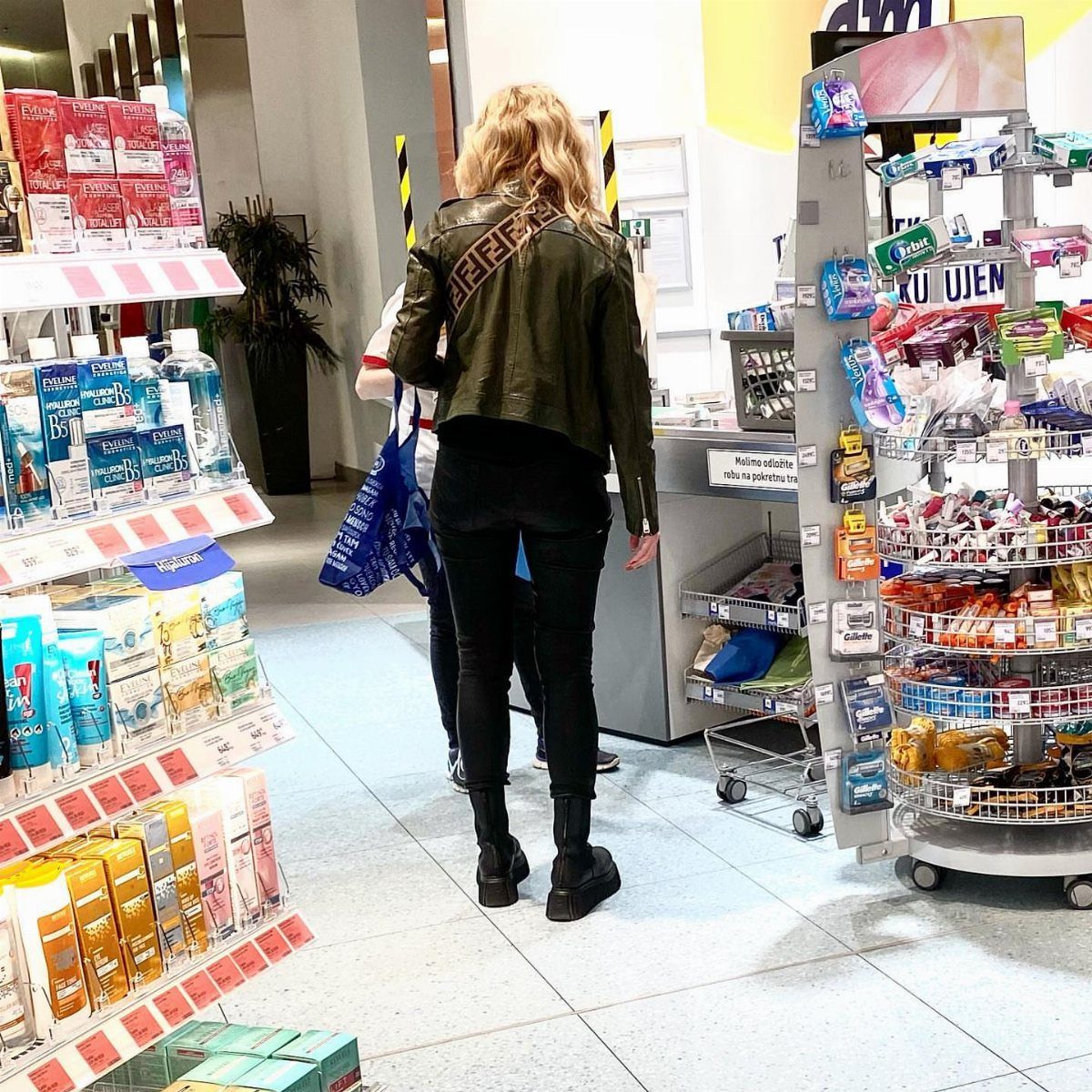 Woman in a leather jacket, black leggings, and black boots walking through a convenience store.