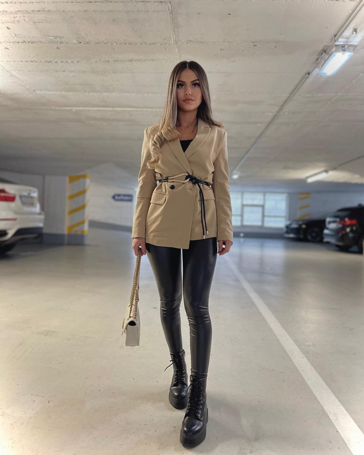 Woman wearing a beige blazer, black leather pants, and black boots in a parking garage.