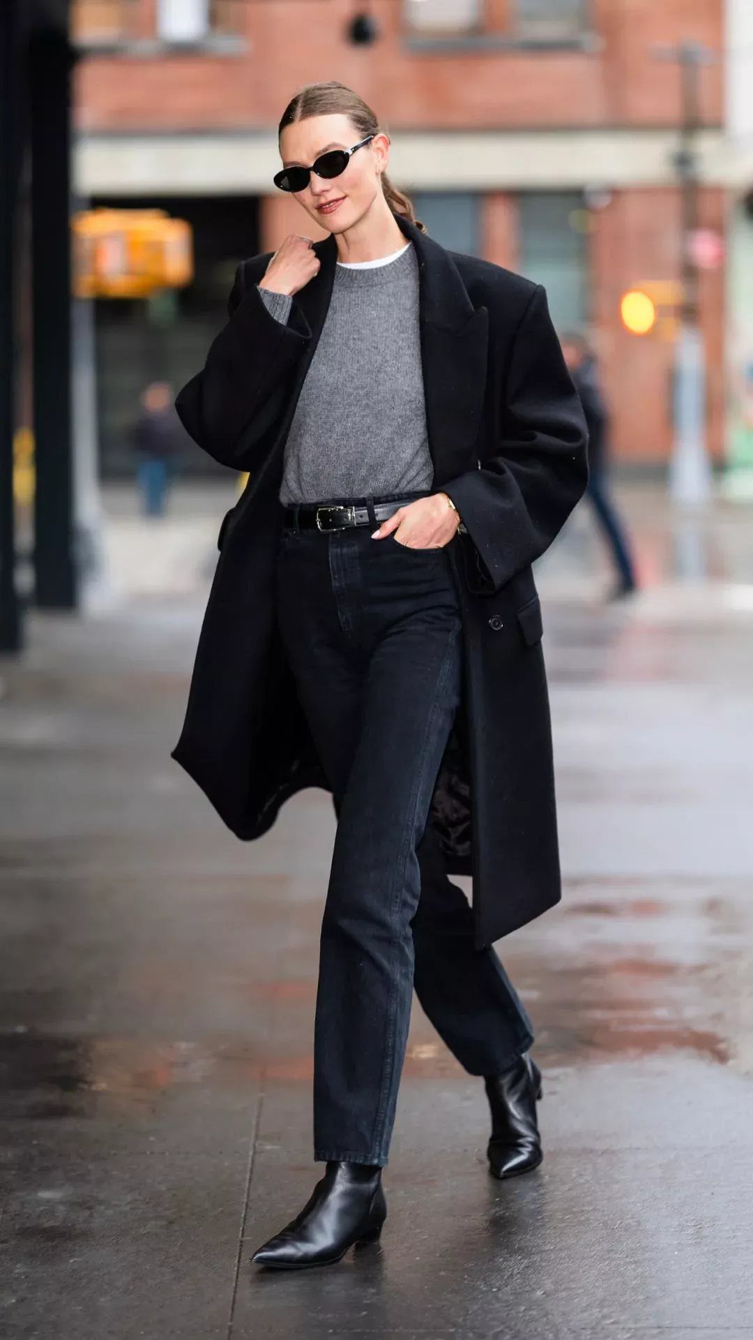 Woman walking in a city wearing black jeans, black ankle boots, and a long black coat.