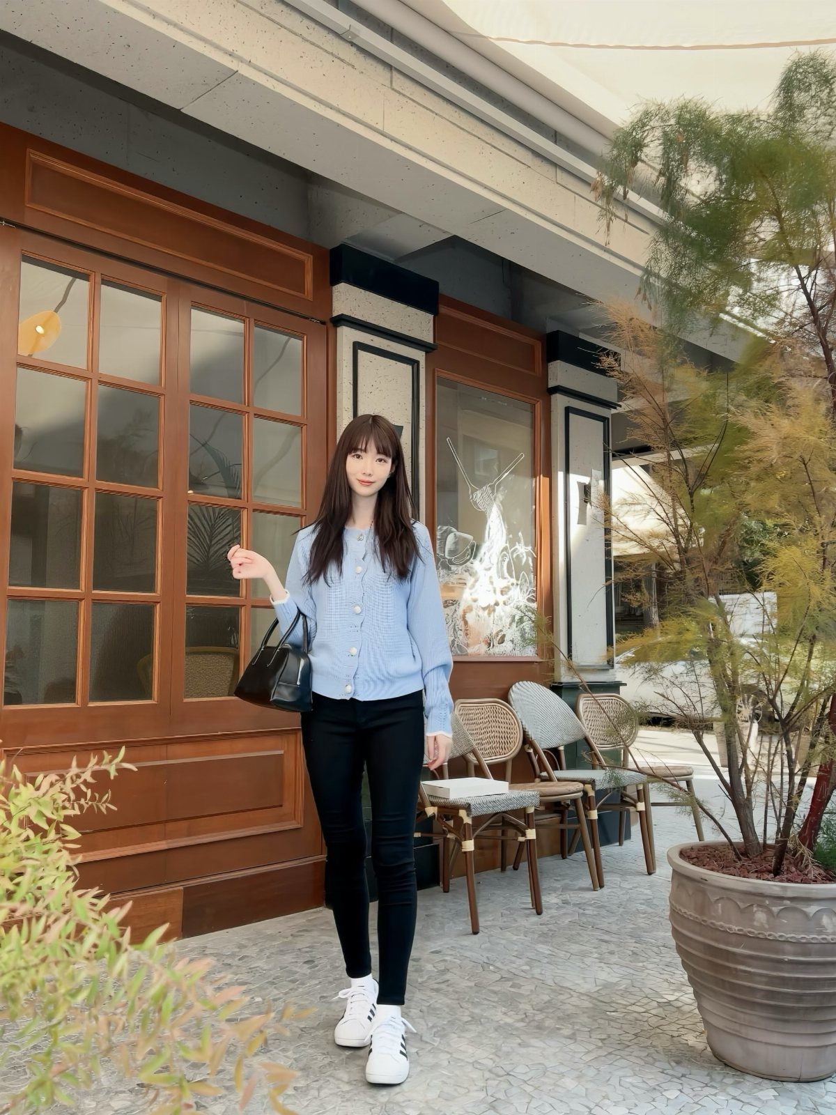 Woman posing in a light blue cardigan, black skinny jeans, and white sneakers outdoors.