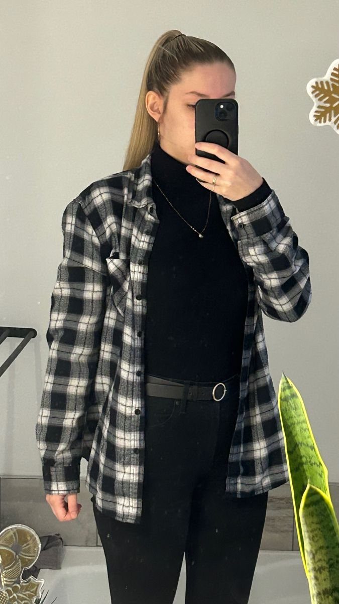Woman in black turtleneck, black pants, and an open black and white plaid flannel shirt.