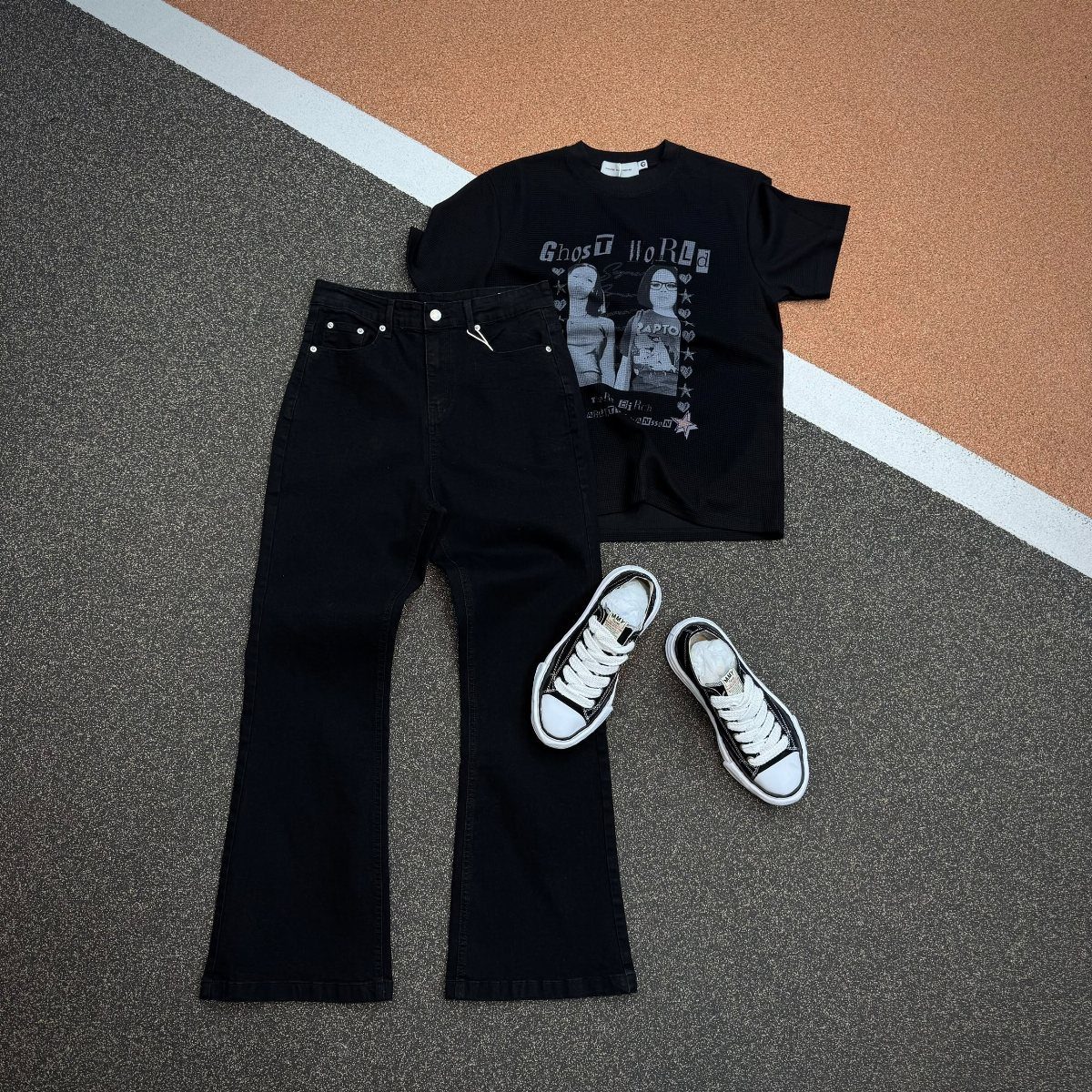 Black flared jeans, a graphic t-shirt, and canvas sneakers laid out on a textured ground.