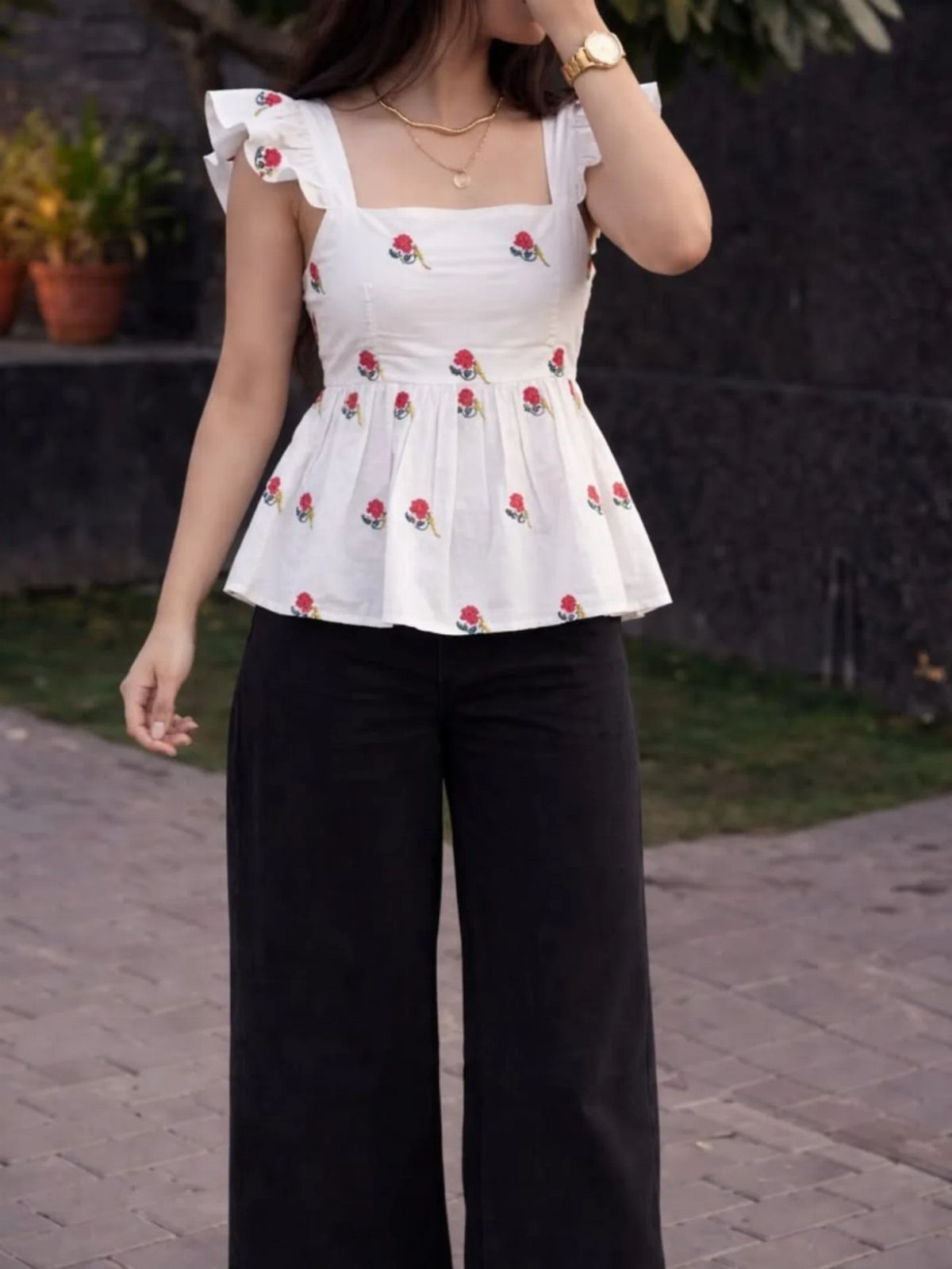 Person wearing black wide-leg jeans and a white floral peplum top outdoors.