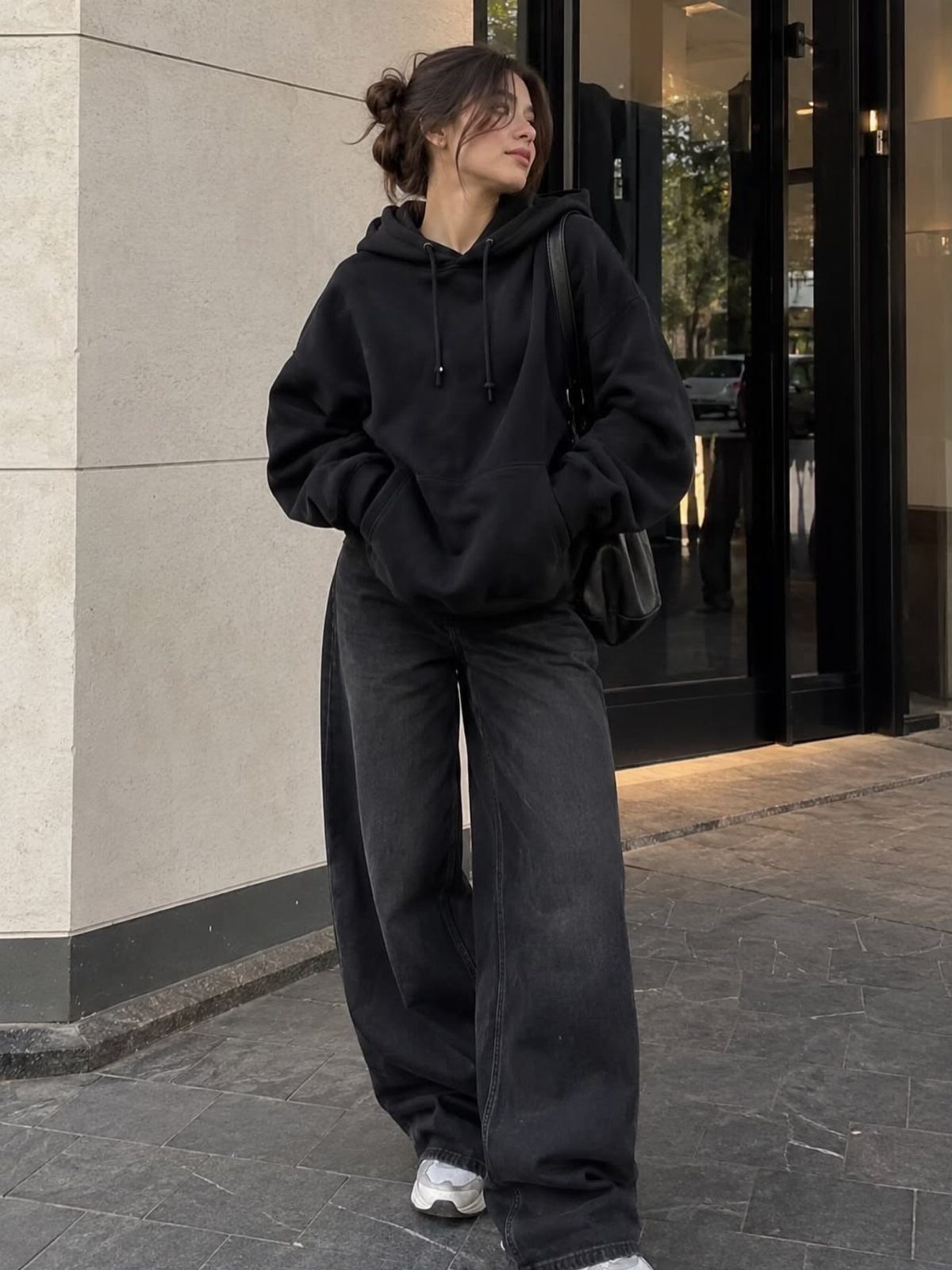Woman wearing a black oversized hoodie and wide-leg black jeans with white sneakers.