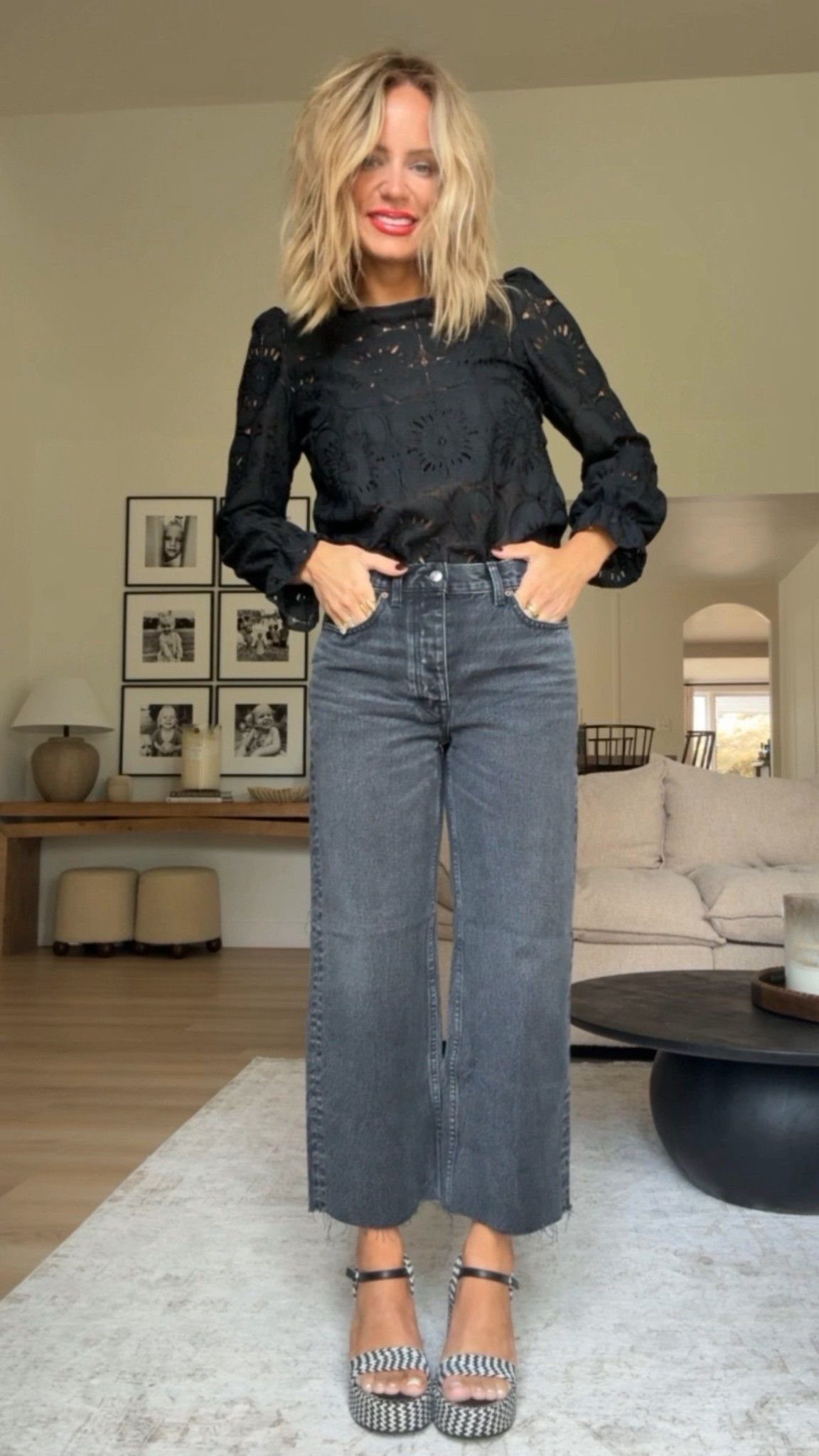 Woman wearing black long-sleeved top, wide-leg black jeans, and striped platform sandals.