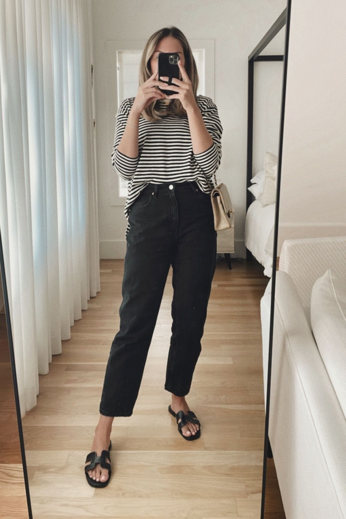 Woman in striped shirt and black jeans posing for a mirror selfie.