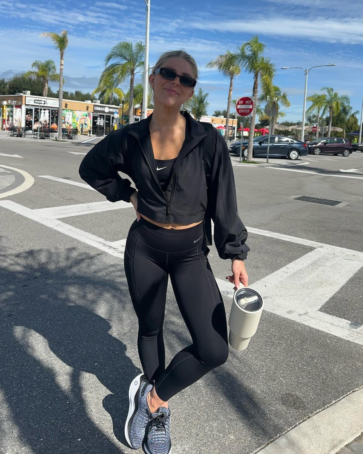 Woman in black leggings and a black cropped zip-up jacket posing on a street.