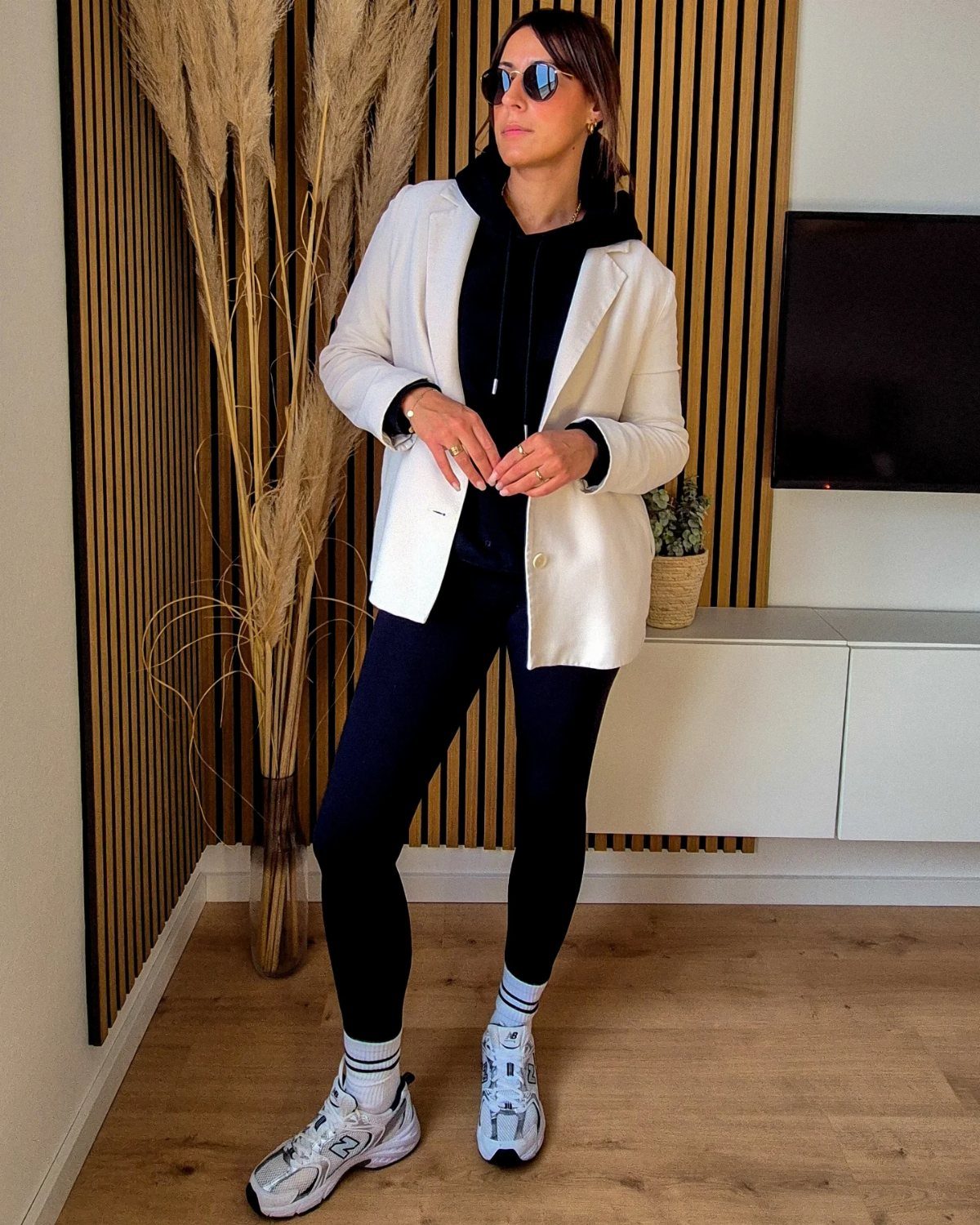 Woman wearing black leggings, a black hoodie, a white blazer, and white sneakers.