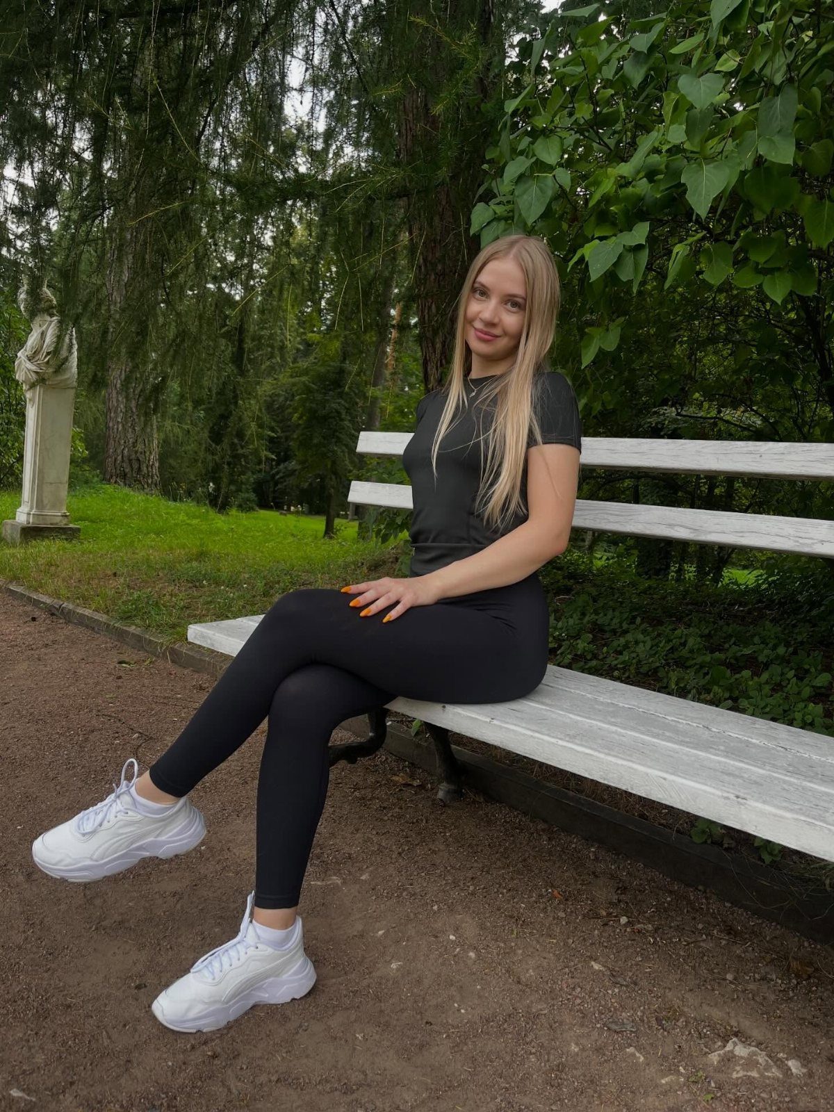 Blonde woman in black leggings and a t-shirt sitting on a park bench.