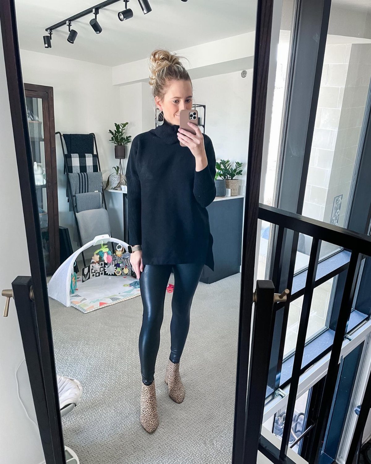 Woman in black turtleneck, shiny black leggings, and leopard print boots posing for a mirror selfie.