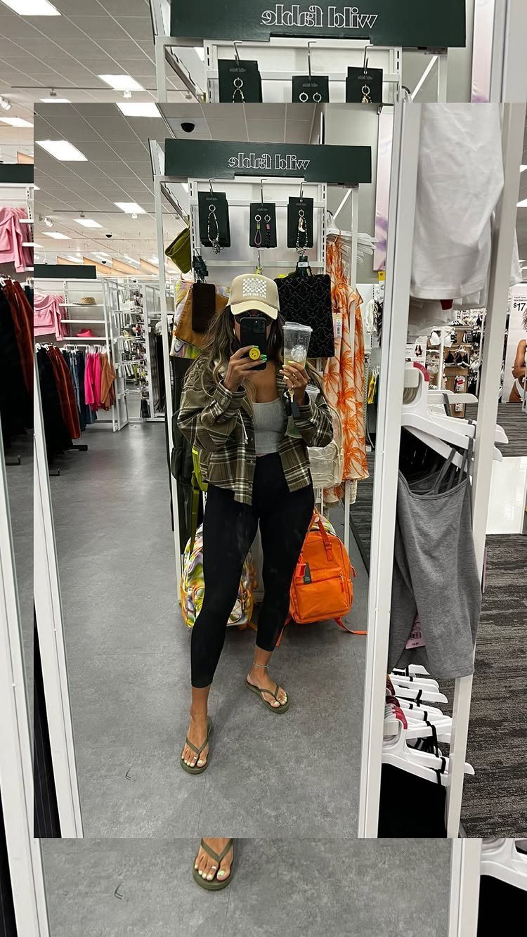 Woman in a clothing store wearing black leggings and an open plaid flannel shirt.