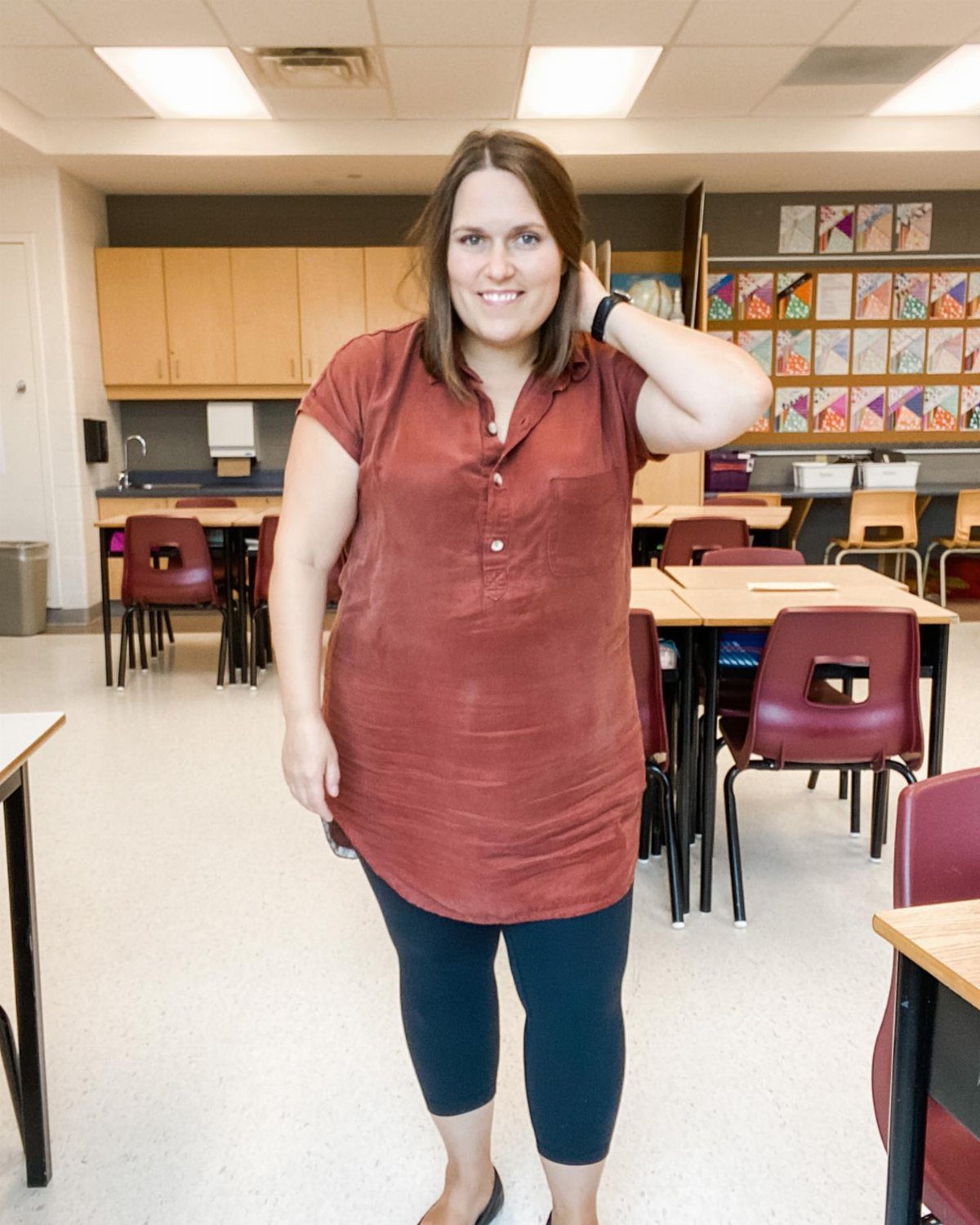 A woman wearing a reddish-brown tunic dress and black leggings in a classroom.