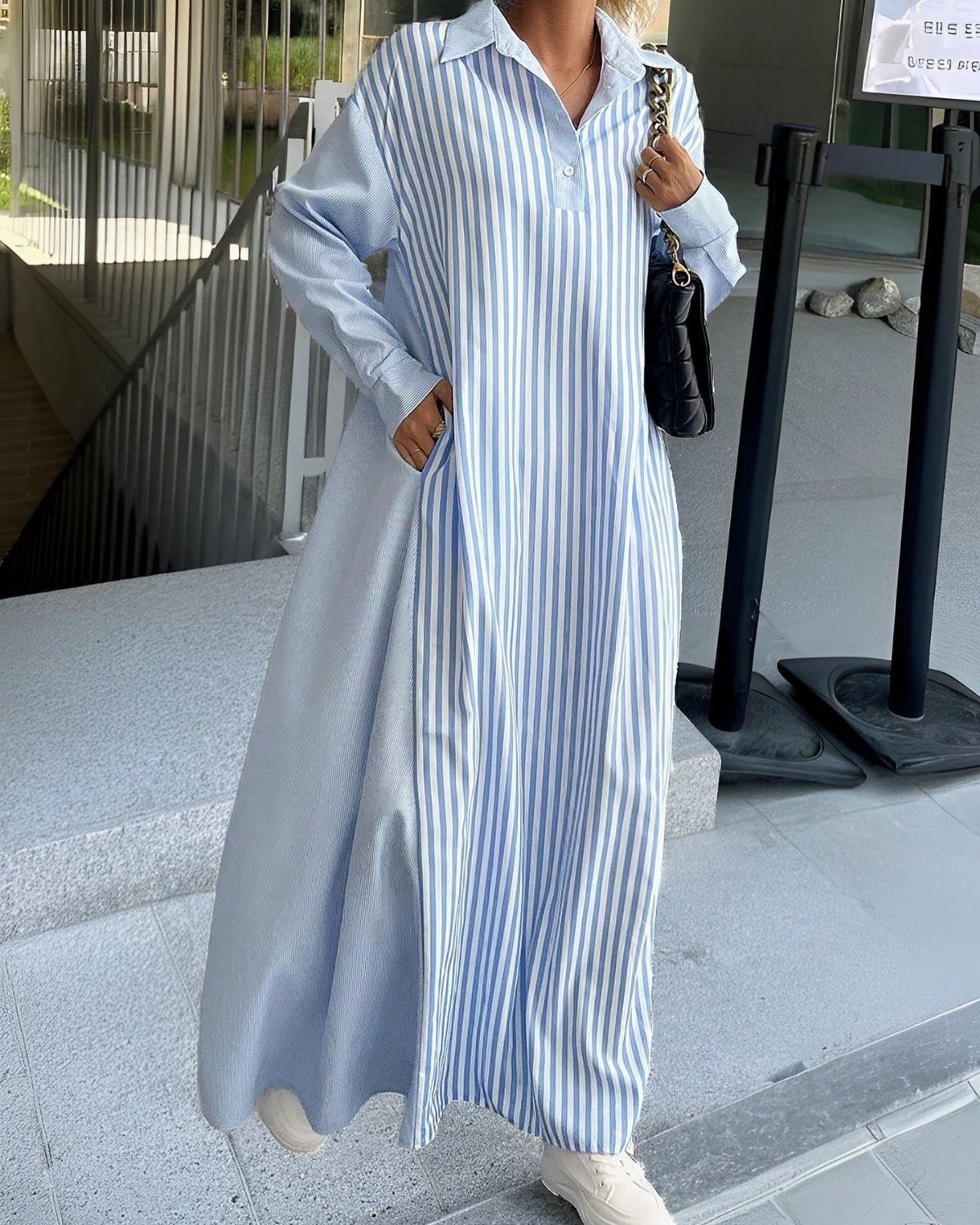 A person wearing a long-sleeved blue and white striped shirt dress and white sneakers.