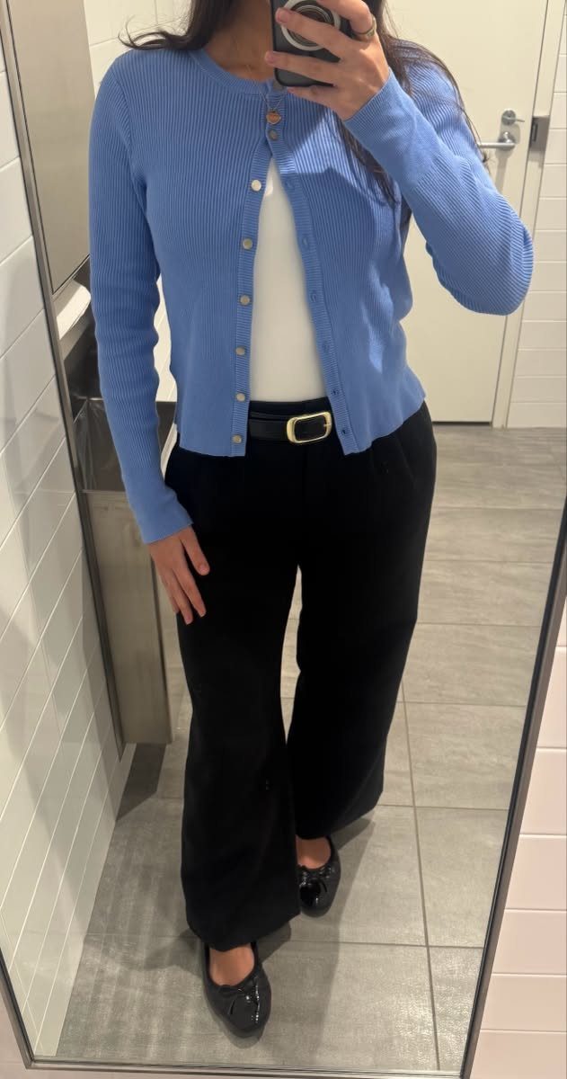 Woman in a blue cardigan, white top, and black wide-leg trousers posing for a mirror selfie.