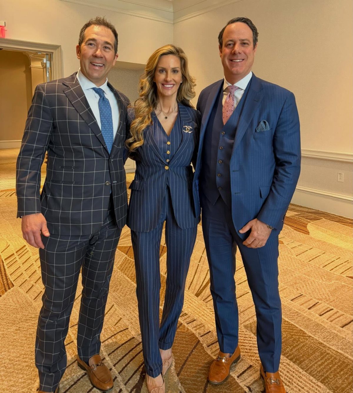 A woman in a navy pinstriped blazer and trousers standing between two men in suits.