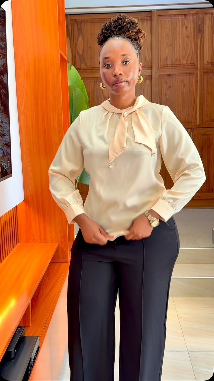 A woman posing in a cream silk bow-neck blouse and black tailored trousers.