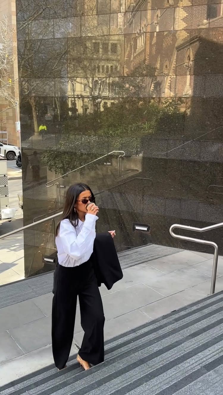 Woman in white blouse and black wide-leg trousers walking down outdoor stairs.