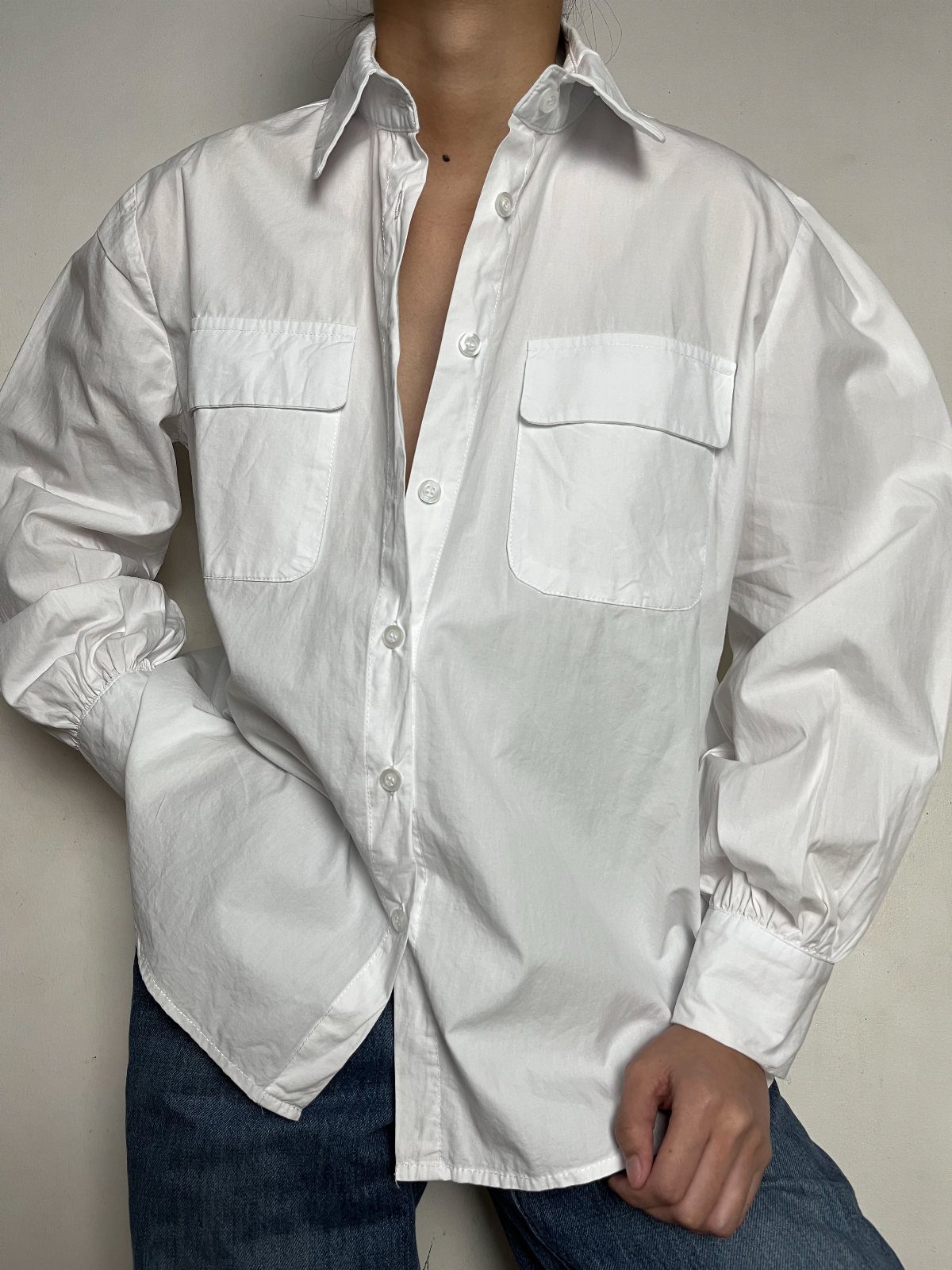 A person wearing an oversized white button-down shirt and blue denim jeans.