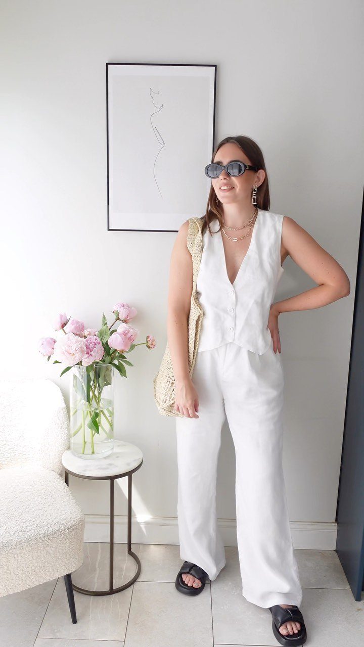 A woman wearing a white linen vest and matching wide-leg trousers standing in a bright room.