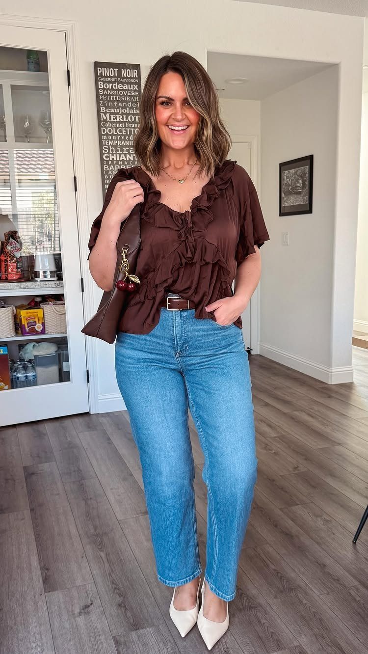 A smiling woman posing in a brown ruffled top and light blue denim jeans.