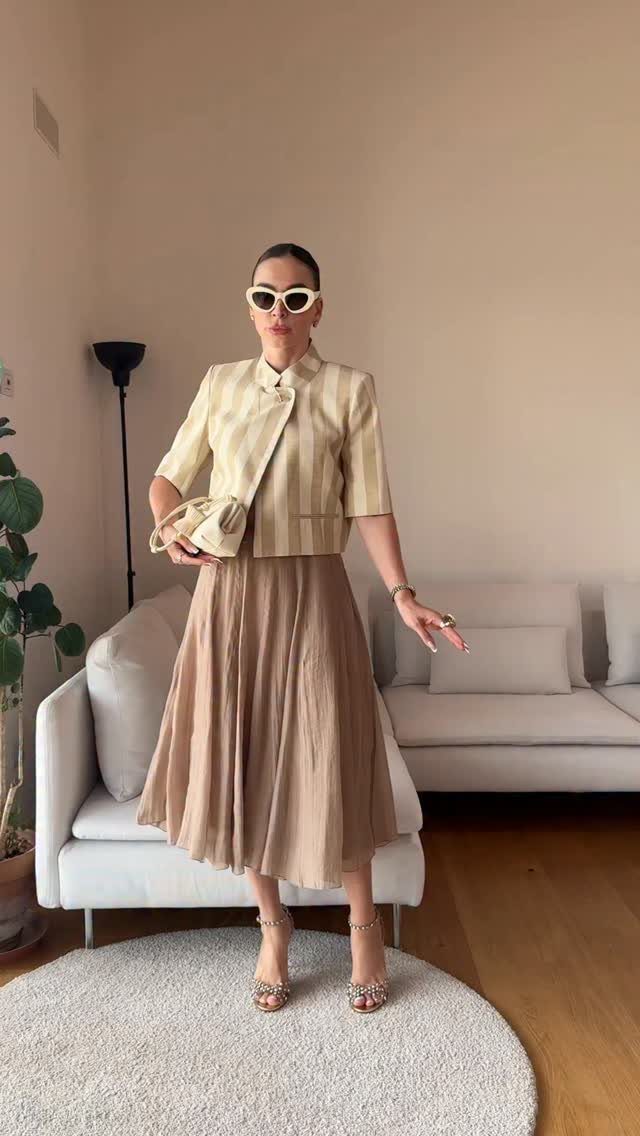 Woman in a beige striped jacket and tan pleated midi skirt standing in a living room.